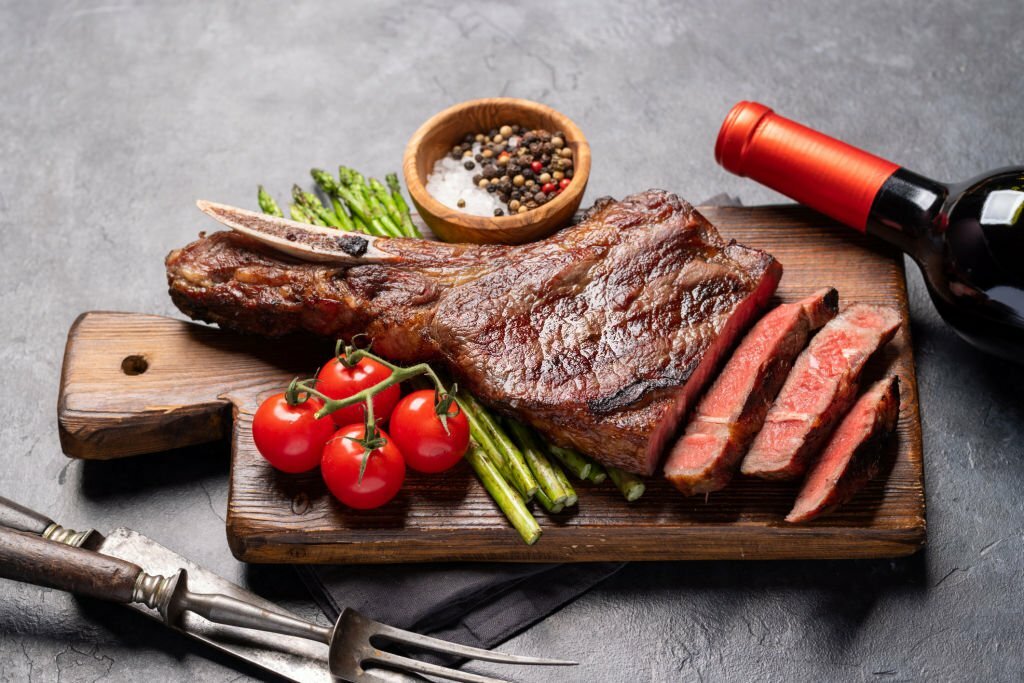 A mouth-watering dish of grilled steak, asparagus, and tomatoes presented on a rustic cutting board.